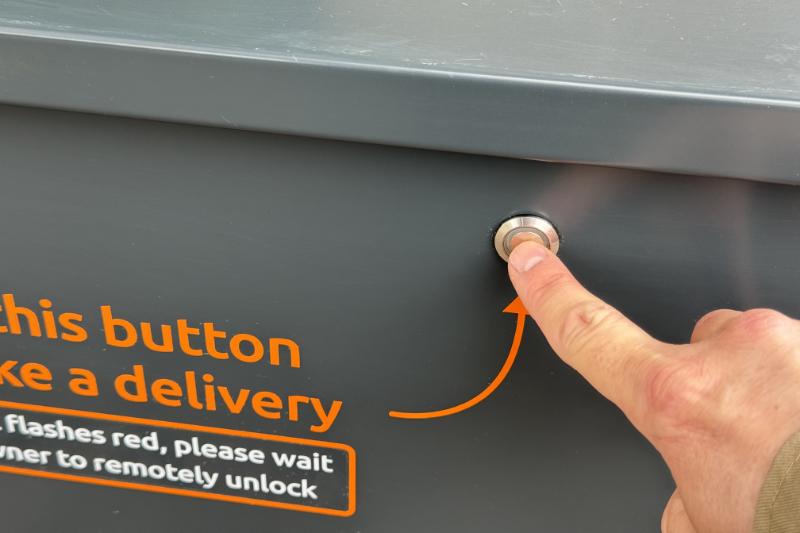 A courier is pressing the button on the front of the iParcelBox smart parcel delivery box to request a delivery